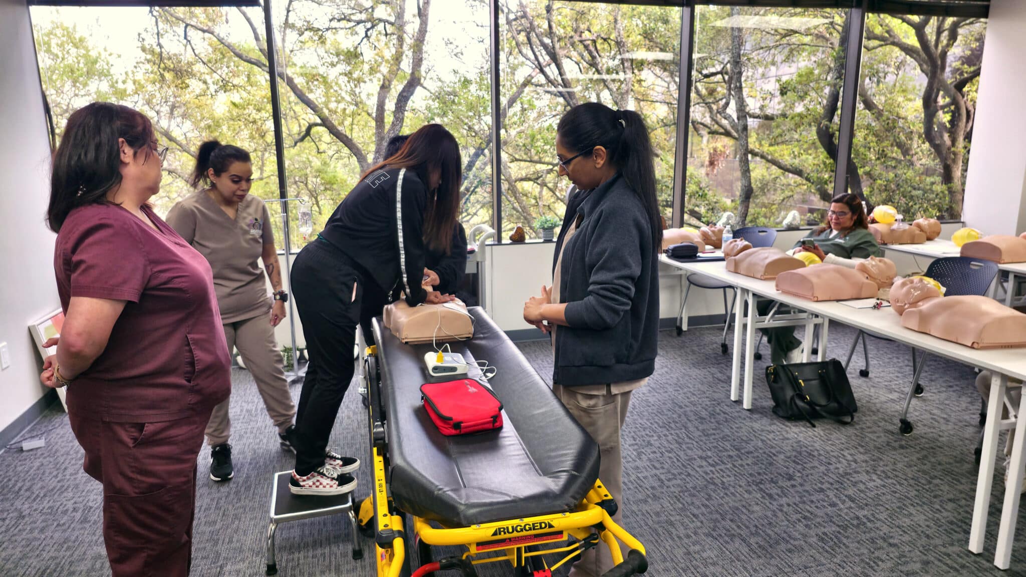 Students performing group-based CPR practice on an adult manikin during a Cardiox Care BLS class in Houston